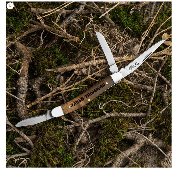 Personalized pocket knife with "Jared Thompson" engraved on the handle, on mossy ground