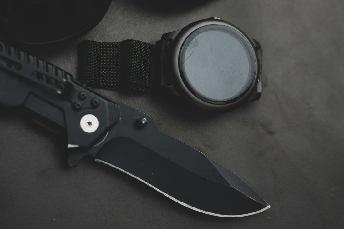 black pocket knife sitting on a table next to a watch